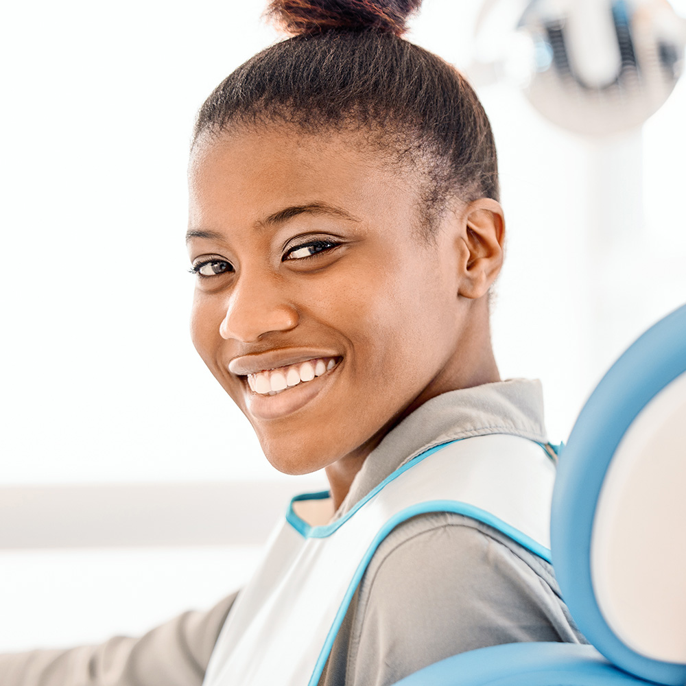 A young woman with a ponytail smiling at the camera while sitting in a dental chair.