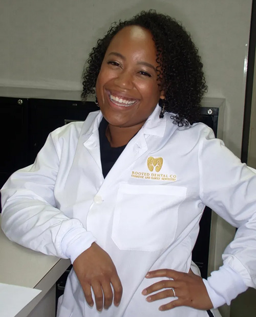 The image shows a person standing behind a counter with a white coat on, smiling at the camera.