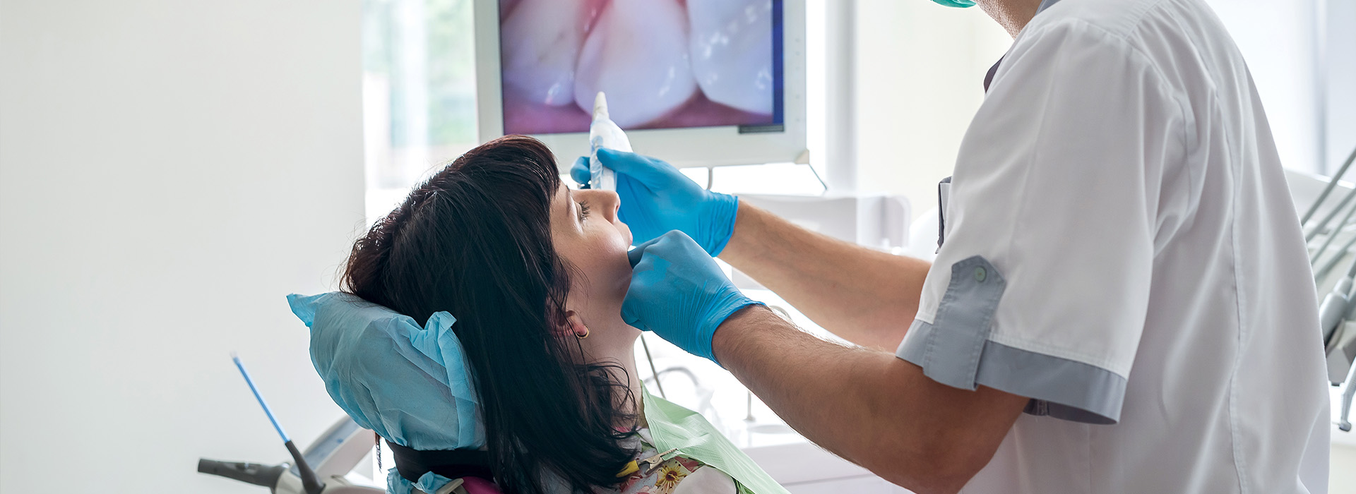 The image shows a dental professional performing a procedure on a patient s mouth while seated in a dental chair.